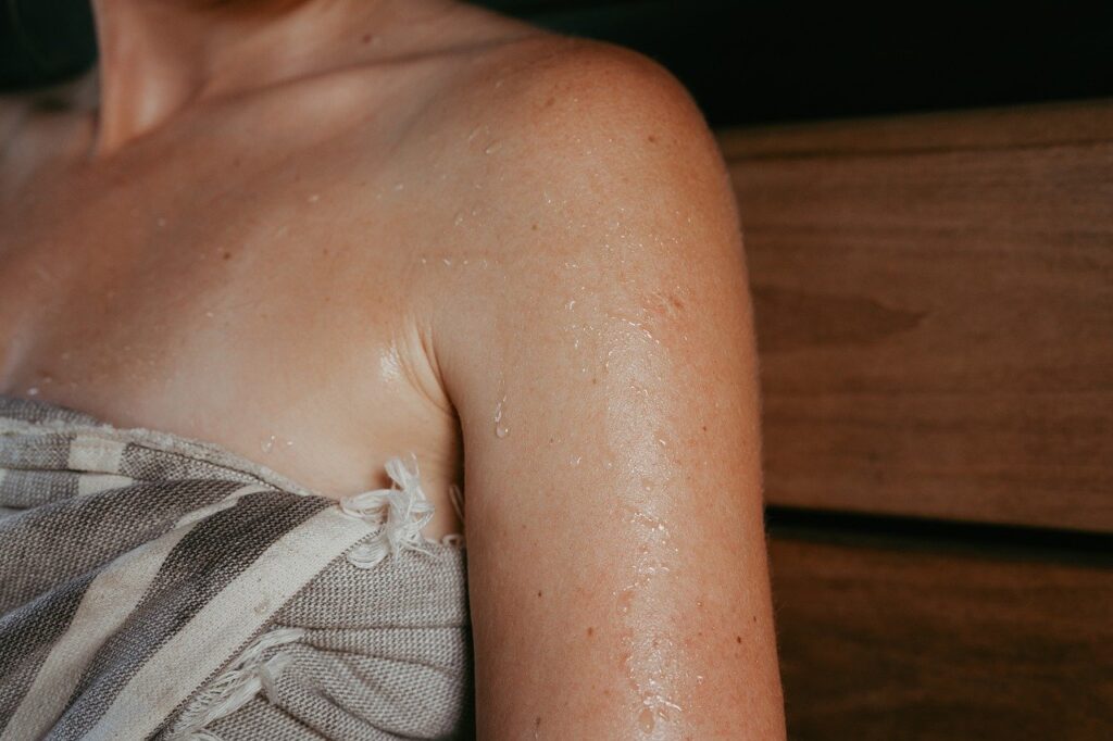 sauna, sauna heater, sauna stones, sauna steam, electric heater, sauna house, sauna design, sauna inspiration, nordic design, safety, safety railing, sauna safety, woman in sauna, sitting in sauna, laughing, person in sauna, sauna bench, pouring water, hive heater, hive mini heater, sauna hat