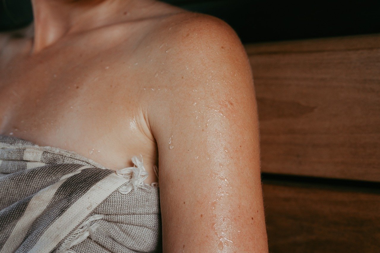 sauna, sauna heater, sauna stones, sauna steam, electric heater, sauna house, sauna design, sauna inspiration, nordic design, safety, safety railing, sauna safety, woman in sauna, sitting in sauna, laughing, person in sauna, sauna bench, pouring water, hive heater, hive mini heater, sauna hat
